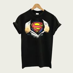 a black t - shirt with a superman logo on the chest and two hands holding it