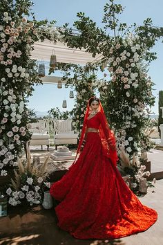 a woman in a red wedding dress standing under an arch with white flowers on it