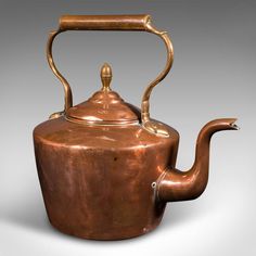 an antique copper teapot with a handle on the side and a curved top is shown against a gray background