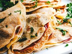 a white plate topped with quesadillas covered in meat and cheese next to parsley