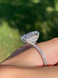 a woman's hand with a diamond ring on top of her finger and grass in the background