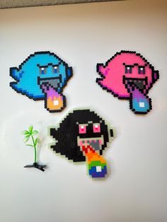 three pixel art pieces sitting on top of a white table next to a plant in a pot