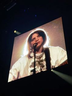 a man with long hair standing in front of a large screen