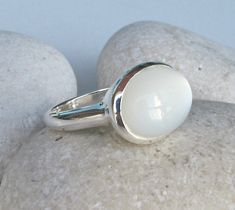 "A Classic Oval shaped Cabochon iridescent White Moonstone Sterling Silver Ring featuring a comfort fit band with a bezel around the stone. The sheen of the white moonstone is what makes this such a striking ring and one of my favorite gemstones. Wrapped in a box ready for gift giving.(r-c-176) FINAL SALE RING INFO ---------------- STERLING SILVER JUNE BIRTHSTONE Stone 14MM(0.55inches) by 18MM (0.70inches) ----> Please note there is an additional fee, if we have to size the ring again so plea White Moonstone Opal Ring In Oval Cabochon Shape, Modern Oval Cabochon Opal Ring, Modern Oval Cabochon Moonstone Ring, White Opal Ring With Oval Cabochon Shape, White Oval Opal Ring With Polished Finish, Modern Moonstone Ring With Oval Bezel Setting, White Moonstone Ring With Oval Cabochon, Modern Oval Moonstone Ring With Bezel Setting, Oval Modern Moonstone Ring With Bezel Setting