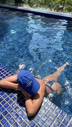 a woman laying on the side of a swimming pool next to a blue tiled wall