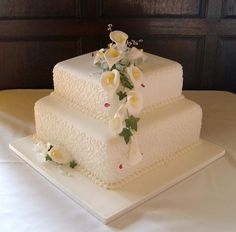 a three tiered cake with white flowers on the top and bottom, sitting on a table