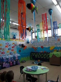 children are sitting around a table in a room decorated with balloons and streamers hanging from the ceiling