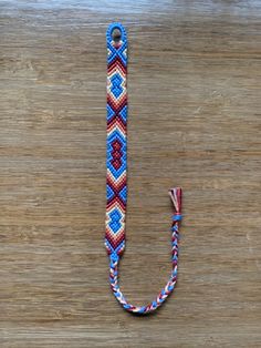 a blue, red and white beaded lanyard on a wooden surface with a hook