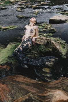 a woman sitting on top of a rock next to a river covered in grass and rocks