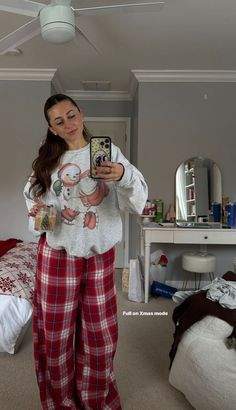 a woman taking a selfie in her bedroom wearing pajamas and holding a cell phone