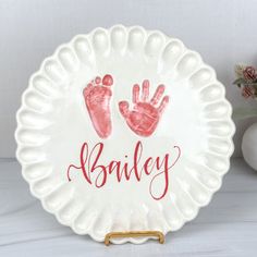 a white plate with red handprints on it and the word bailey written in pink