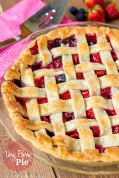 a close up of a pie on a table with strawberries and blueberries in the background