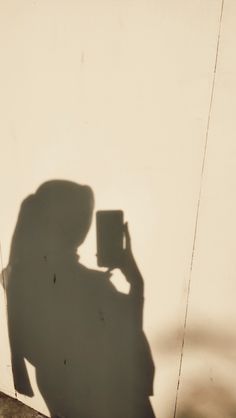 the shadow of a person holding a cup in front of their face, with a wall behind them