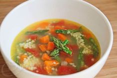 a white bowl filled with vegetable soup on top of a wooden table