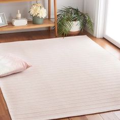 a large white rug on the floor in a room with wooden floors and shelves filled with plants