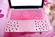 a cat laying on top of a bed next to a pink laptop computer with leopard print