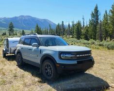 a silver truck parked on top of a dry grass field next to trees and mountains