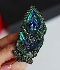 a hand holding a brooch with an intricate design on it