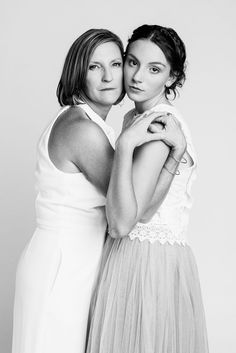 two women are hugging each other while posing for a black and white photo in front of a gray background