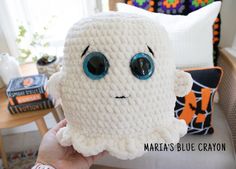 a person holding up a crocheted stuffed animal with big blue eyes and nose