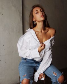 a woman sitting on top of a wooden chair wearing ripped jeans and a white shirt