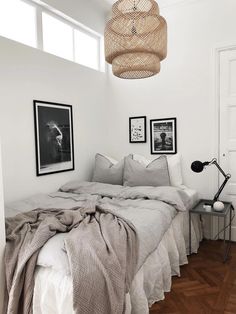 a bedroom with white walls and wood flooring is pictured in this image, there are pictures on the wall above the bed