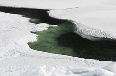 an aerial view of some water in the middle of snow covered ground and ice floes