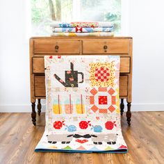 a table with a quilt on it next to a wooden dresser and window sill