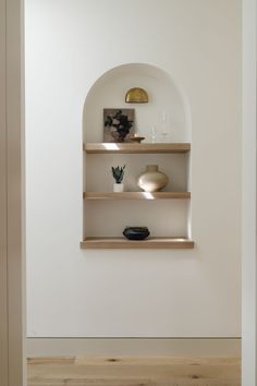 two shelves with vases and pictures on them in a white walled room, along with wood flooring