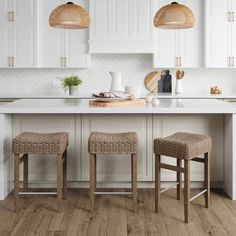 three stools in front of a kitchen island with white cabinets and wood flooring