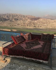 a bed sitting on top of a metal rail next to a lush green hillside covered in mountains