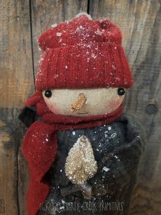 a small stuffed animal with a red hat and scarf on it's head, standing in front of a wooden wall