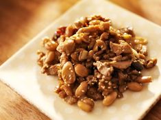 a white plate topped with meat and beans on top of a wooden table next to a fork