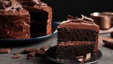 a slice of chocolate cake on a plate with the rest of the cake in the background