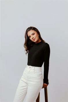 a woman in white pants and black top posing for the camera with her legs crossed