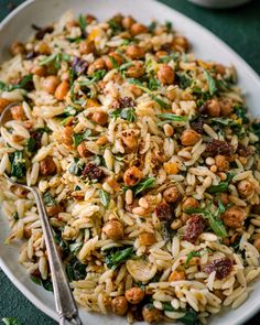 a white bowl filled with pasta and nuts on top of a green table cloth next to a fork