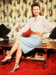 a woman sitting on top of a wooden table in front of a floral wallpaper