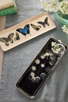 two trays with butterflies on them sitting on a table next to flowers and books