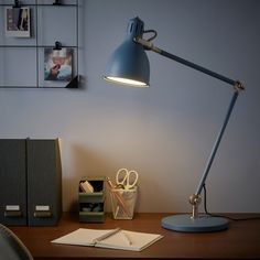 a desk lamp sitting on top of a wooden table next to a notebook and pen