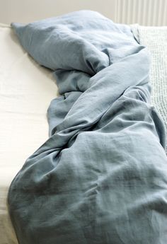 an unmade bed with blue sheets and pillows