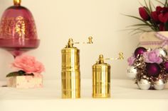 two golden salt and pepper shakers sitting on top of a table next to flowers