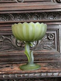 a green glass vase sitting on top of an old wooden table next to a wall