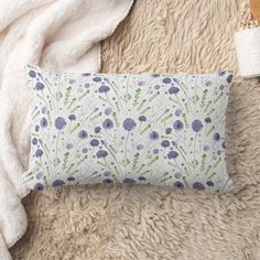 a pillow with purple flowers on it sitting on a fluffy white rug next to a blanket