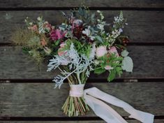 a bouquet of flowers tied to a white ribbon on top of a wooden table with wood planks