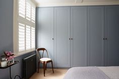 a bedroom with blue walls and white bedding has a chair next to the window