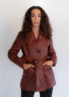 "Vintage 70s belted leather coat. The stand out on this bohemian classic is the oversized collar, buttons, and back pleated stitch detail. Wide wing collar. Long sleeves with wide cuffs. Front pockets. Front sash belt. Back waist panel with stitch detail. Large front button fastening. Fully lined. We kindly ask that you please view all measurements for comparison so you can get your desired fit. * Brand: Junior Gallery * Decade: 1970s * Fabric: 100% Leather * Lining: Satin * Color: Rustic Red C Vintage Leather Outerwear For Fall, Vintage Long Leather Jacket For Fall, Vintage Red Leather Outerwear, Retro Belted Fall Outerwear, Retro Belted Outerwear For Fall, Winter Leather Jacket With Belt, Brown Vintage Outerwear For Fall, Brown Vintage Fashion Outerwear For Fall, Brown Outerwear For Fall Vintage Fashion