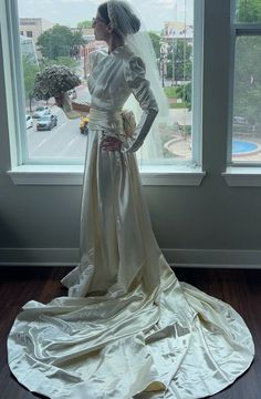 a woman standing in front of a window wearing a wedding dress