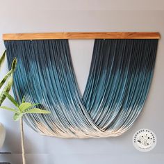 a blue and white wall hanging next to a plant in a vase on a table