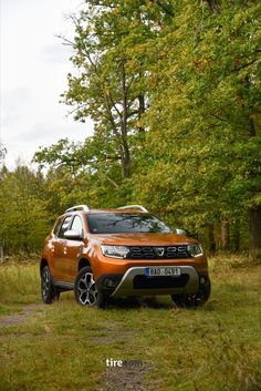 an orange dacia parked in front of some trees