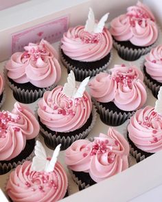 cupcakes with pink frosting and white decorations in a box on a table